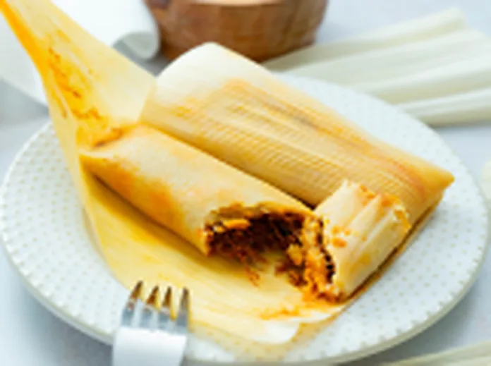 A chicken tamale on a plate, cut open to show the masa and seasoned filling