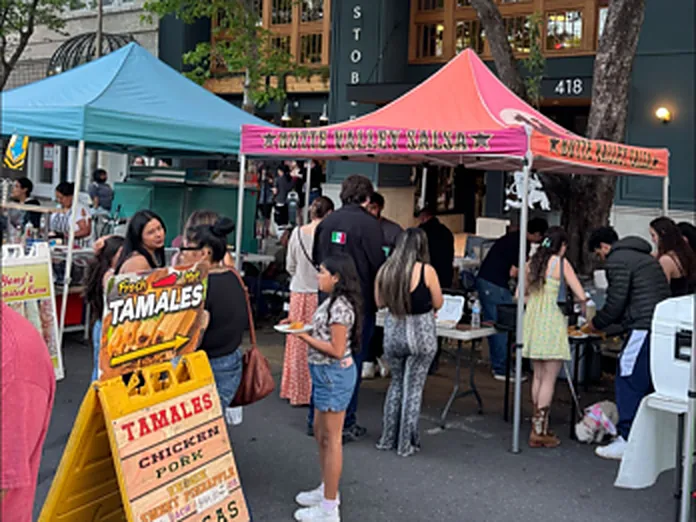A busy street market at dusk with canopies, a tamales sign and shoppers