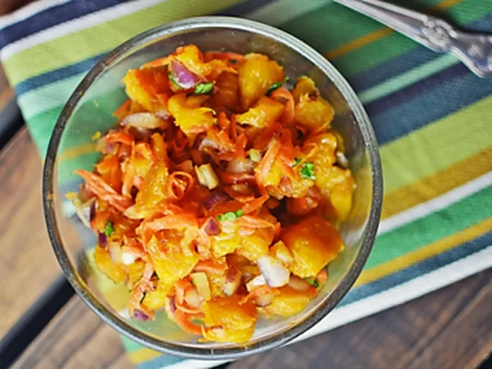 A glass bowl of mild orange salsa with diced onion and herbs on a striped cloth