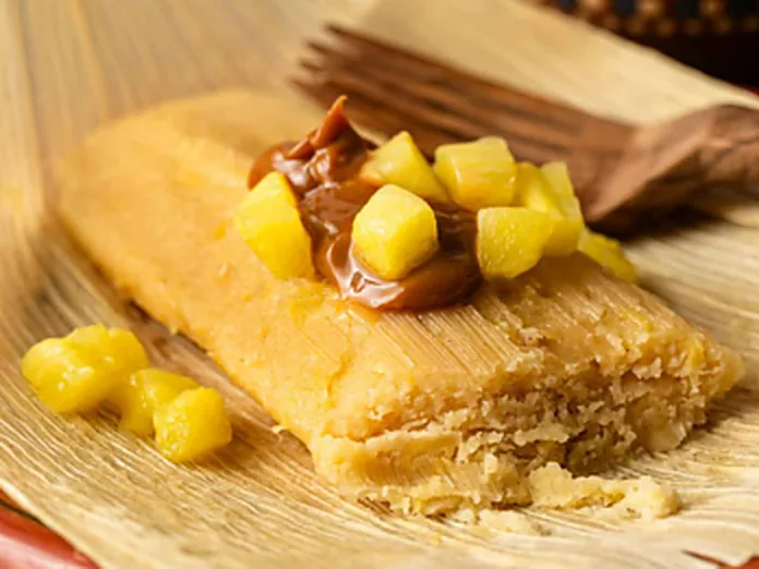 A sweet tamale topped with pineapple pieces and caramel sauce on a corn husk