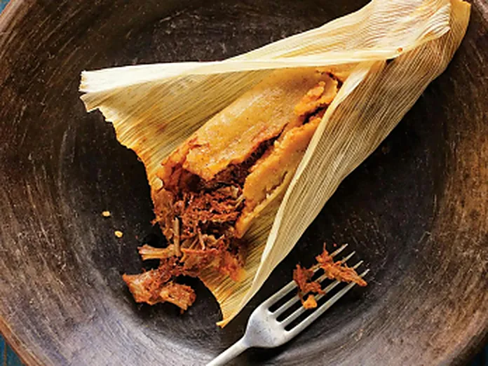 A pork tamale opened in its corn husk showing seasoned shredded pork filling