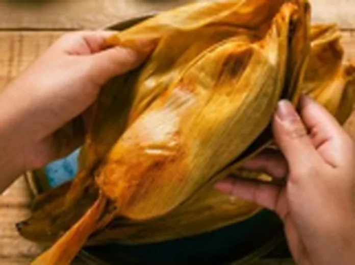 Hands folding a tamale closed inside its corn husk